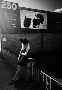 Full length of woman sitting on railing against wall