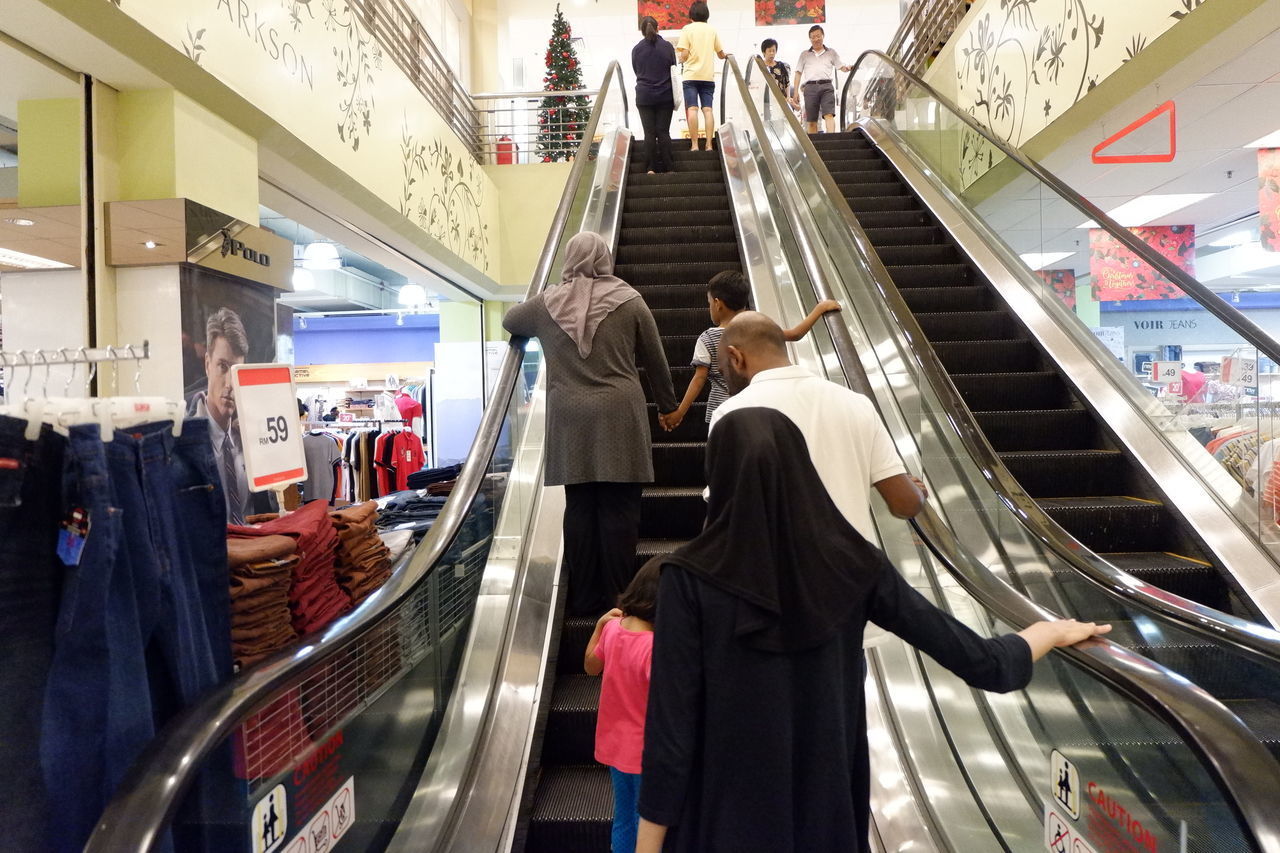 REAR VIEW OF PEOPLE STANDING ON ESCALATOR AT STORE