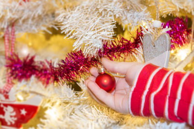 Cropped hand of child holding bauble hanging on christmas tree at home