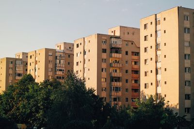 Low angle view of trees by apartment buildings against sky