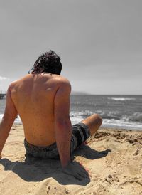 Rear view of shirtless man sitting at beach