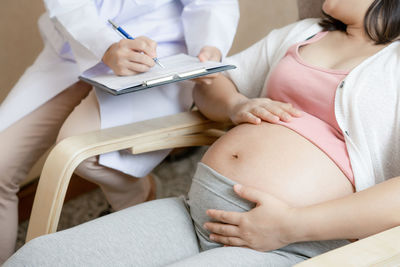 Midsection of doctor with pregnant woman at home