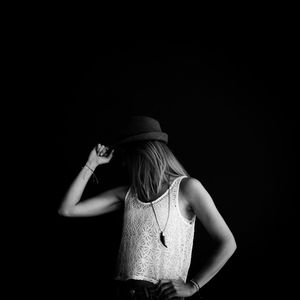 Woman with covered face wearing hat against black background