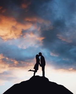 Low angle view of silhouette man kissing woman while standing against sky during sunset