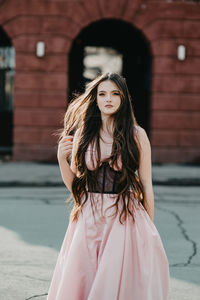 Portrait of a girl in a pink dress with long brown hair standing outdoors 