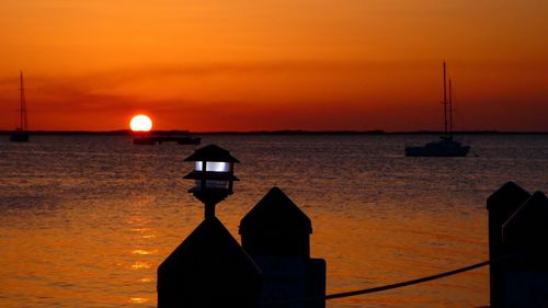 Silhouette sailboat on sea against orange sky