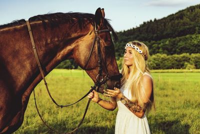 Woman feeding grass to horse on field