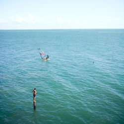 Boy looking at person windsurfing in sea against sky