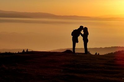 Silhouette couple kissing on field against sky during sunset