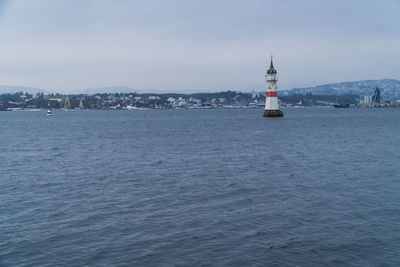 Lighthouse on sea against buildings in city