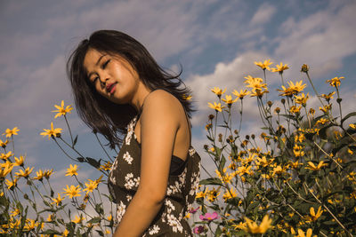 Beautiful young woman standing amidst flowering plants on field against sky