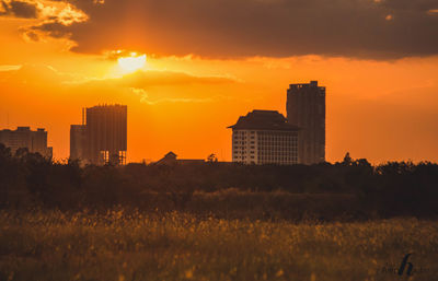 Buildings on field against orange sky