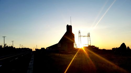 Silhouette of factory against sky at sunset