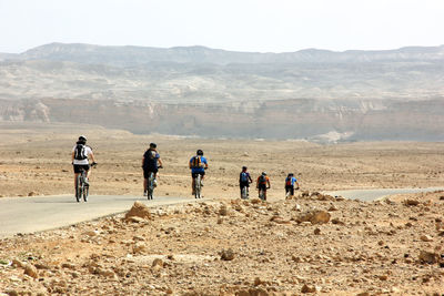 Rear view of people cycling against mountains