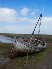 Abandoned boat moored on shore against sky