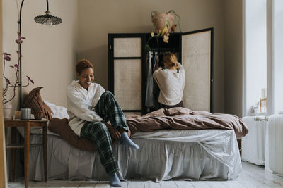 Smiling non-binary person wearing socks while sitting on bed at home