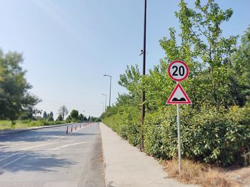 Road sign by street against sky