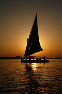 Silhouette ship in sea against orange sky