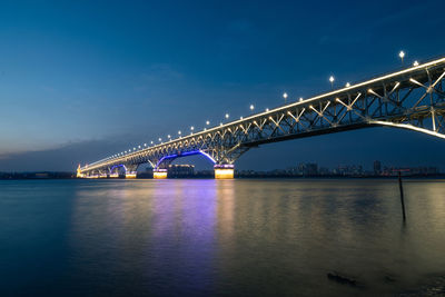 Illuminated bridge over river against sky at night