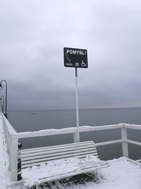 Information sign by sea against sky during winter