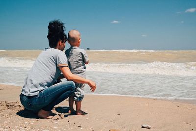 Mother with son at shore against sky