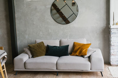 Grey sofa with pillows, round mirror hanging on the wall in a modern scandinavian-style living room