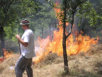 Side view of man standing by burning hay at forest