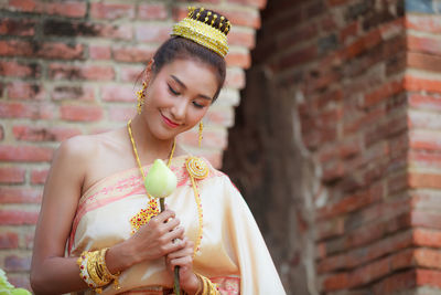 Young woman wearing sari holding flower against brick wall