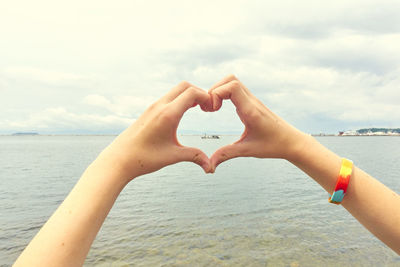 Midsection of man making heart shape against sea against sky