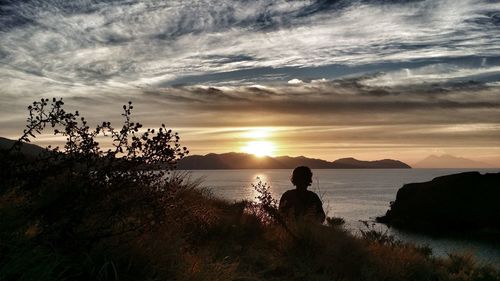 Silhouette people on sea against sky during sunset