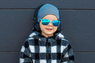 Portrait of boy wearing sunglasses standing against wall outdoors