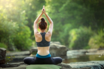 Rear view of woman doing yoga while sitting on rock