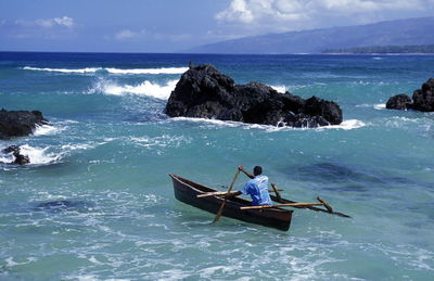 Man rowing outrigger on sea against rock formation