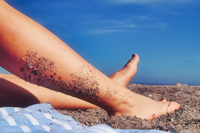 Low section of woman relaxing on beach against sky