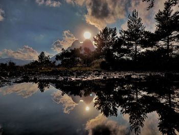 Reflection of silhouette trees in lake against sky