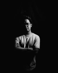 Portrait of young man with arms crossed standing against black background