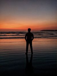 Rear view of silhouette man standing on beach against sky during sunset