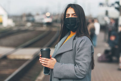 Portrait of woman holding smart phone while standing in city