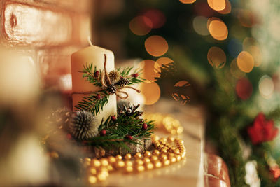 A candle in a christmas candlestick stands on a shelf or fireplace, close-up.