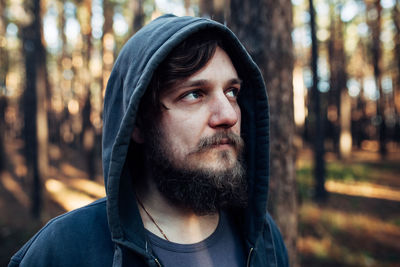 Close-up of mid adult man wearing hood looking away in forest