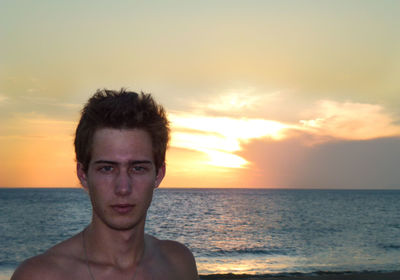 Portrait of shirtless man at beach against sky during sunset
