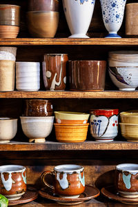 Various pottery ceramic displayed on wooden shelves at store.