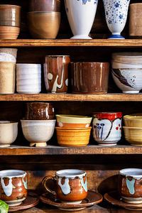 Various pottery ceramic displayed on wooden shelves at store.