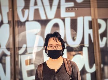 Young man in eyeglasses and face mask standing in front of alphabet letters on large led screen.