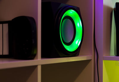 A sub woofer with green light on around speaker on the room shelf