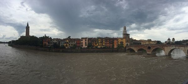 Arch bridge over river by buildings against sky