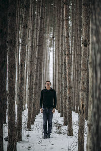 Young man stands tall among snow covered pine tree forest in maine