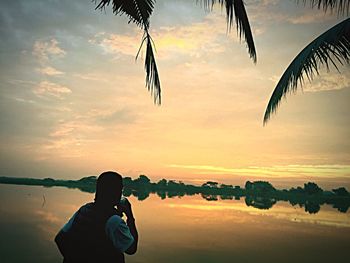 Man photographing sea against sky during sunset