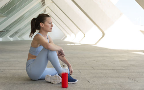 Sporty, fit woman sitting relaxing with a bottle of water after exercise, urban background.