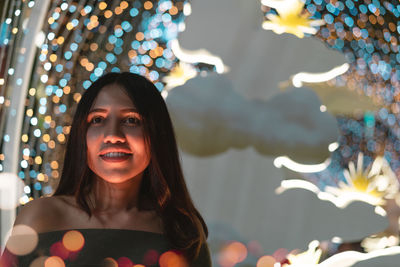 Smiling young woman looking away against illuminated lights